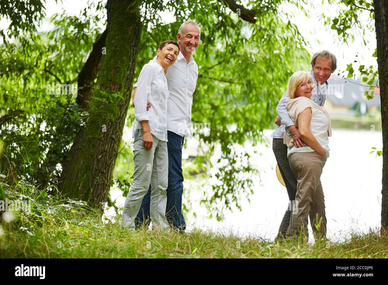 Zwei Paar lachende Senioren machen einen Spaziergang um ein see im Sommer Stockfoto