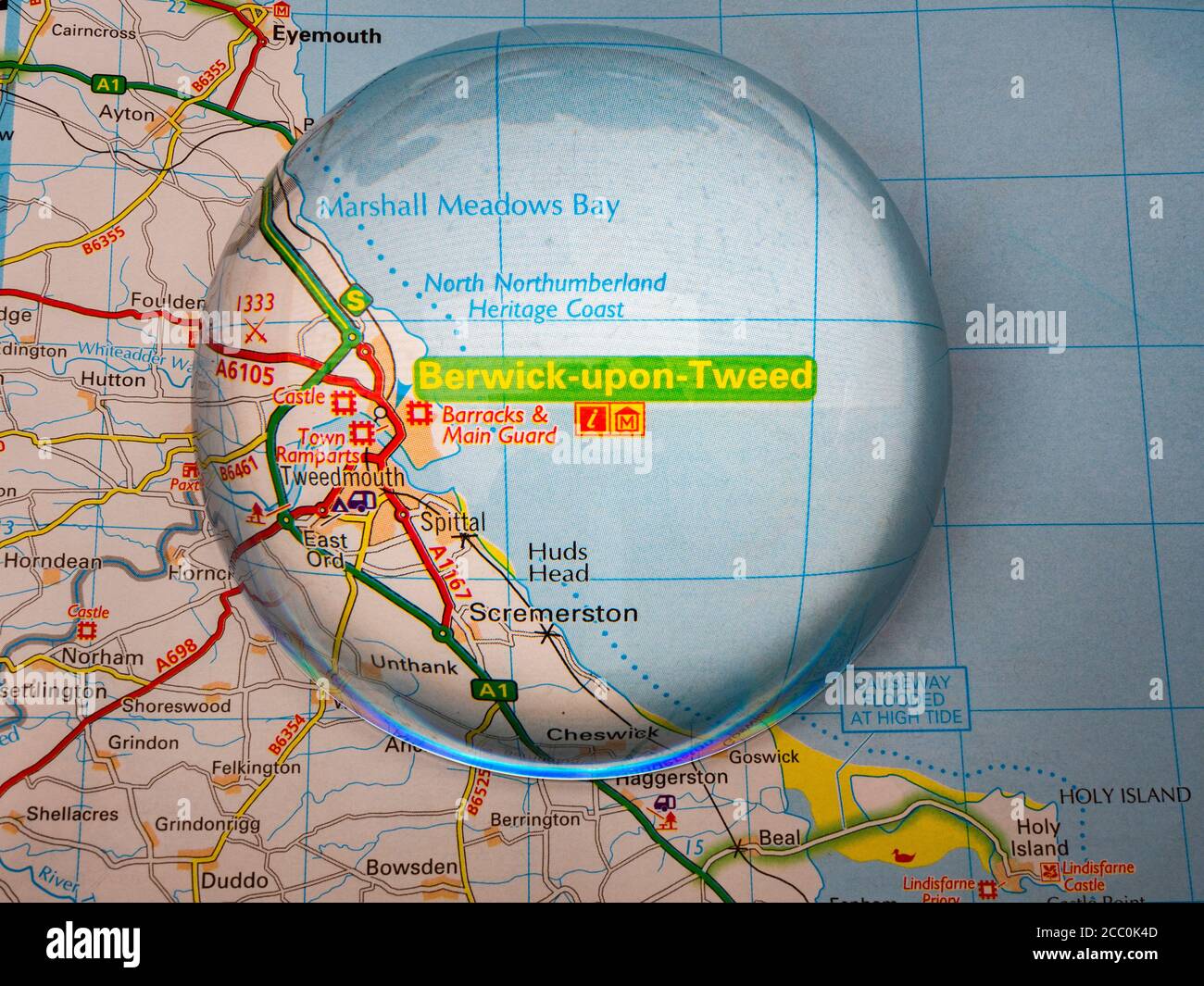 Nahaufnahme einer Kuppellupe über einer Seite einer britischen Straßenatlas-Karte, mit der Berwick upon Tweed-Gegend von England für eine genauere Ansicht vergrößert. Stockfoto