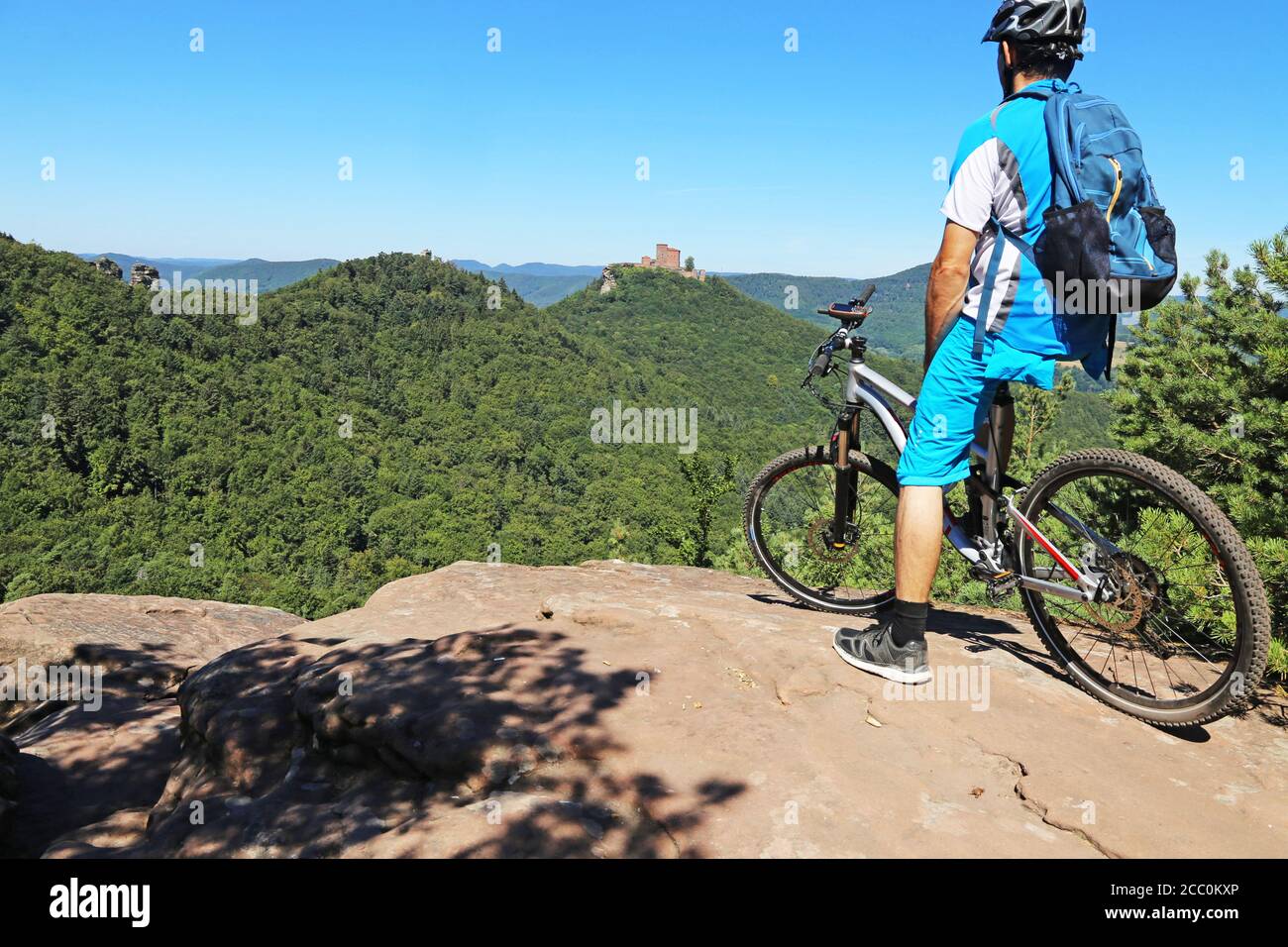 Symbolbild: Mountainbiker auf einem Felsen im Pfälzer Wald mit Blick auf Schloss Trifels, Annweiler (Modell erschienen) Stockfoto