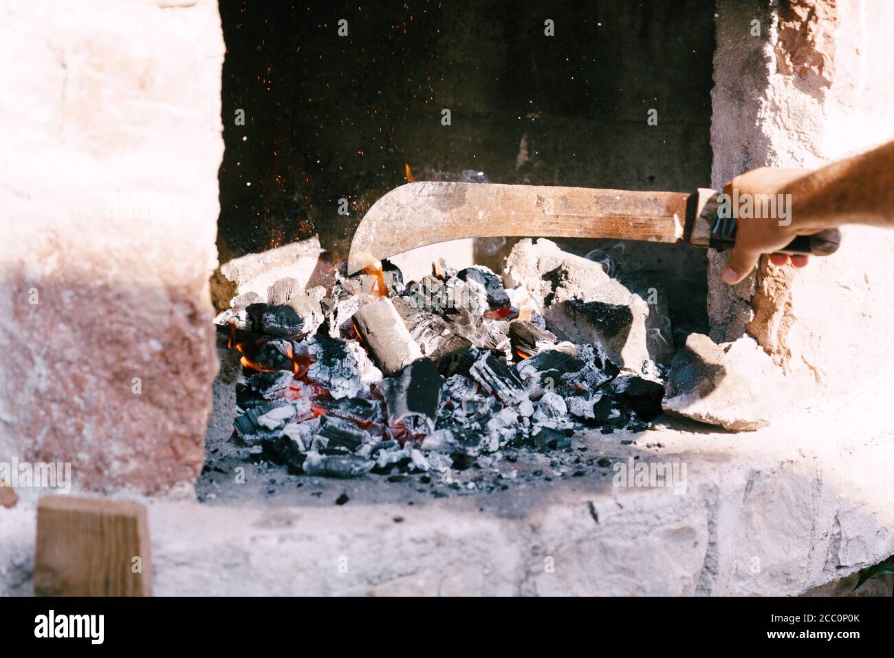 Der Koch legt brennende Kohlen mit einer Machete in den Grill. Stockfoto