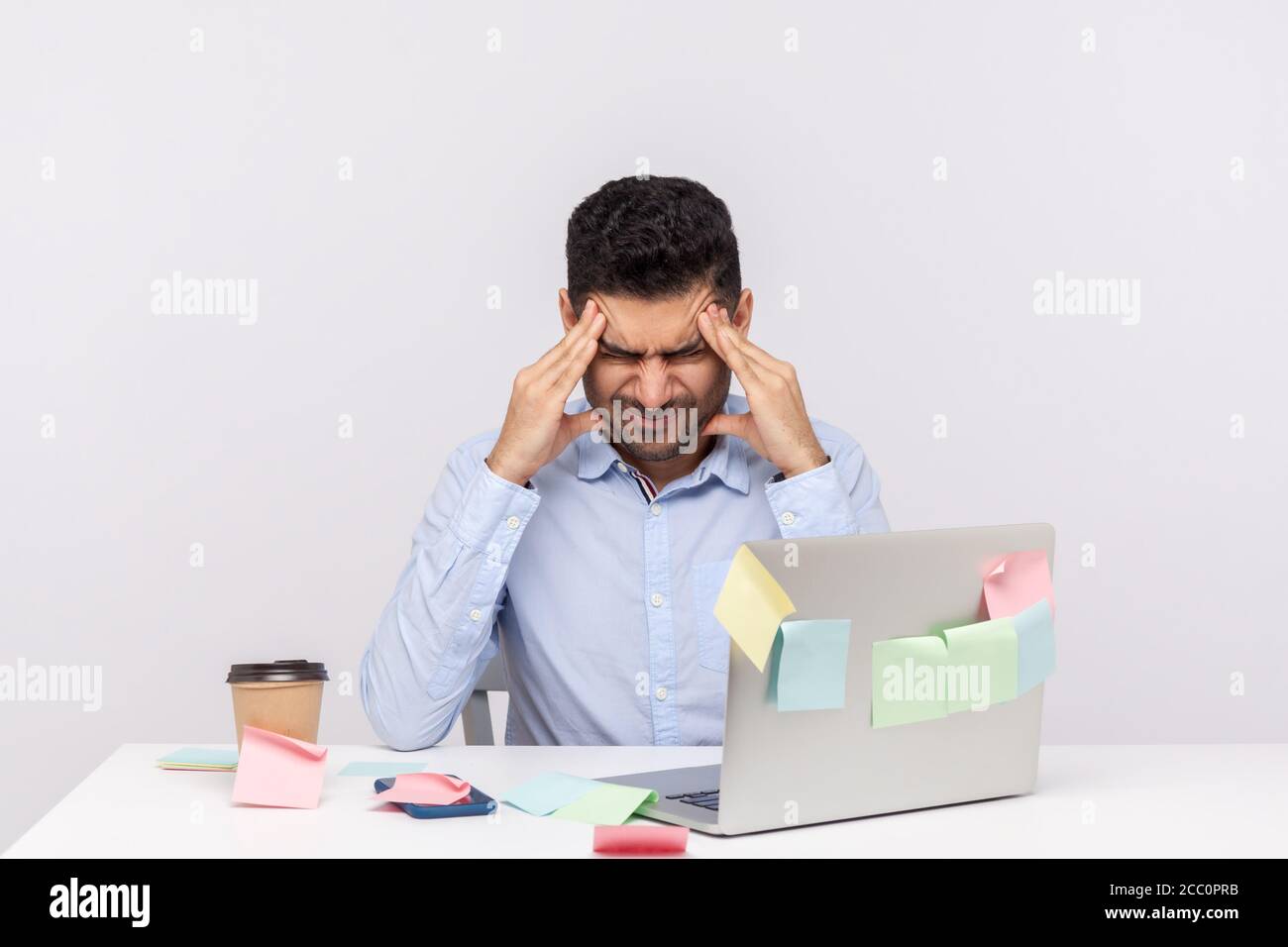 Migräne von stressigen Job. Deprimierter Mann Mitarbeiter sitzt im Büro, klammernden Kopf Tempel, leiden Kopfschmerzen und Anspannung, besorgt über Probleme bei Stockfoto