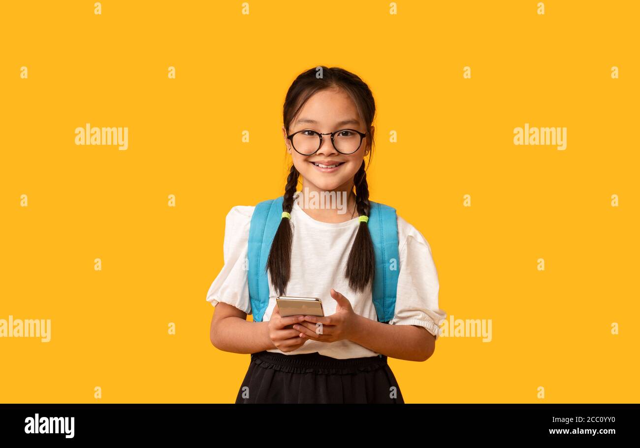 Chinesisch Schulmädchen Mit Handy Stehen Über Gelben Hintergrund, Studio Stockfoto