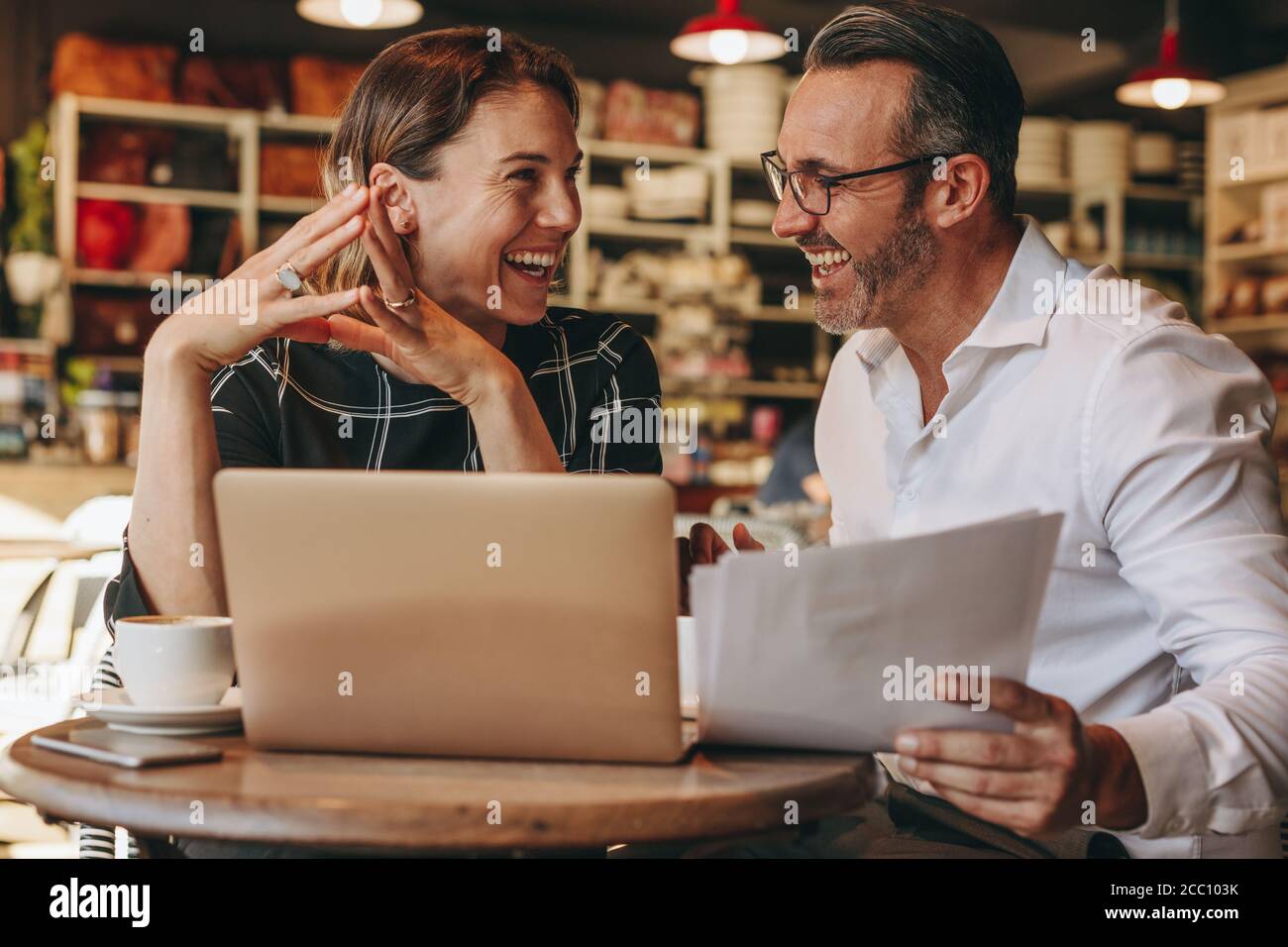 Lächelnder Geschäftsmann und Geschäftsfrau, die im Café mit Laptop und Dokumenten sitzen. Geschäftsleute, die im Café arbeiten. Stockfoto