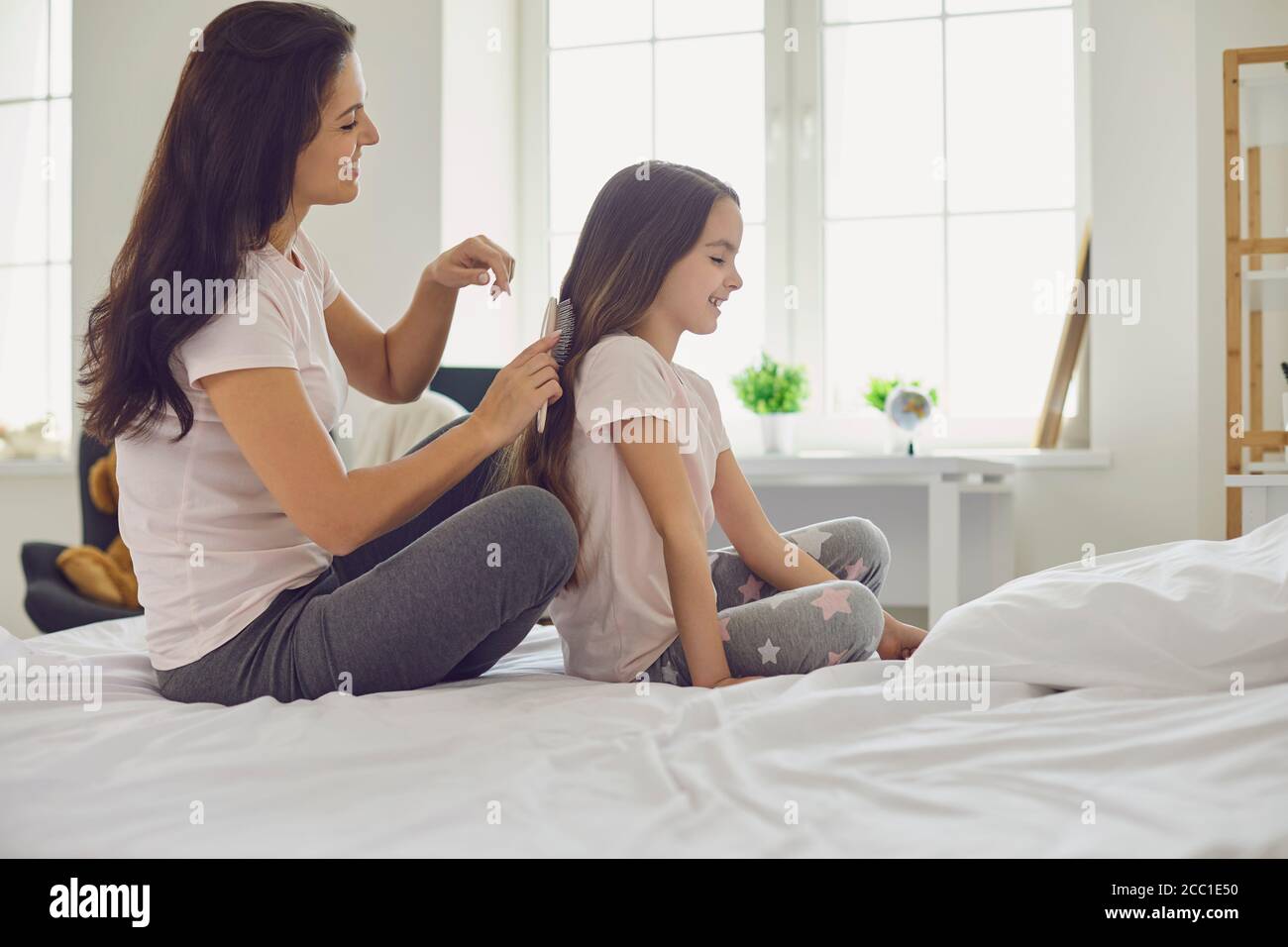 Mutter macht Frisur zu Mädchen Kind auf dem Bett im Schlafzimmer sitzen. Stockfoto