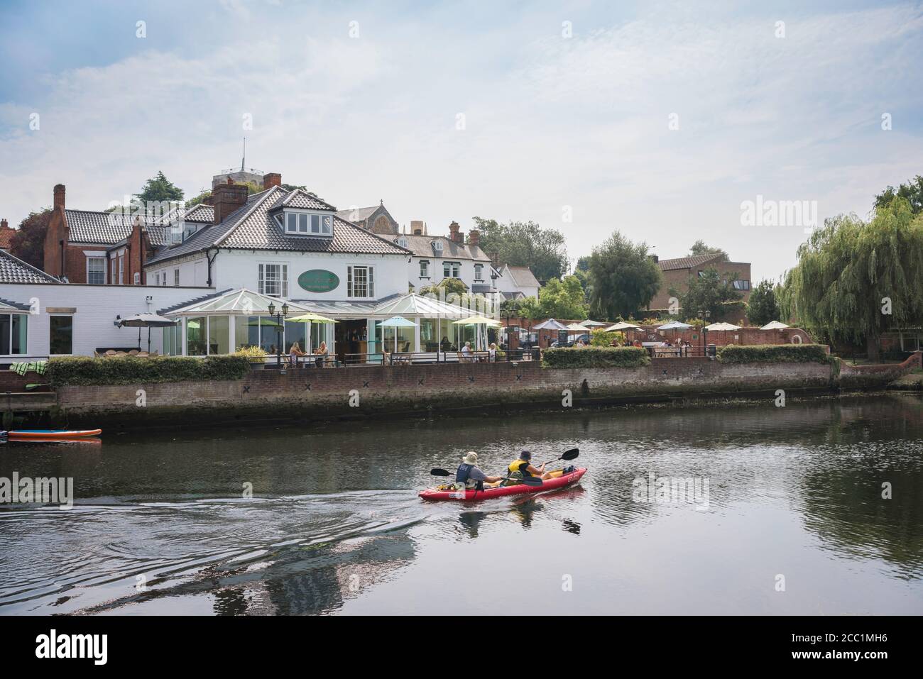 Ehepaar mittleren Alters, Rückansicht eines reiferen Paares in einem Kanu, das an einer Hotelterrasse am Flussufer in Suffolk, England, vorbeirudert Stockfoto