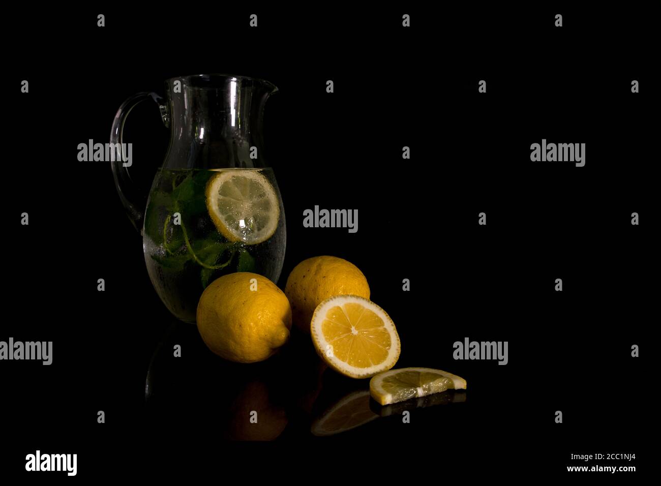 Stillleben mit einem Krug mit Wasser gefüllt mit Minze Und Zitrone mit der rohen Zitronenfrucht im Vordergrund Stockfoto