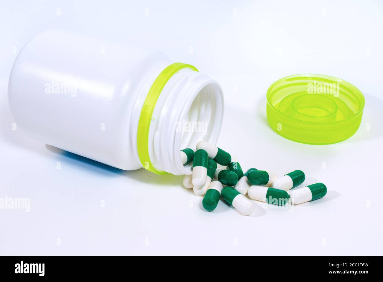 Grüne Arzneitabletten innen und außen eine weiße Plastikflasche auf weißem Hintergrund. Stockfoto