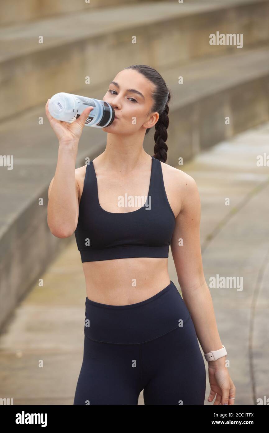 Porträt einer athletischen jungen Frau, die von einem Getränk trinkt Flasche trägt Leggings und Sport-BH Stockfoto