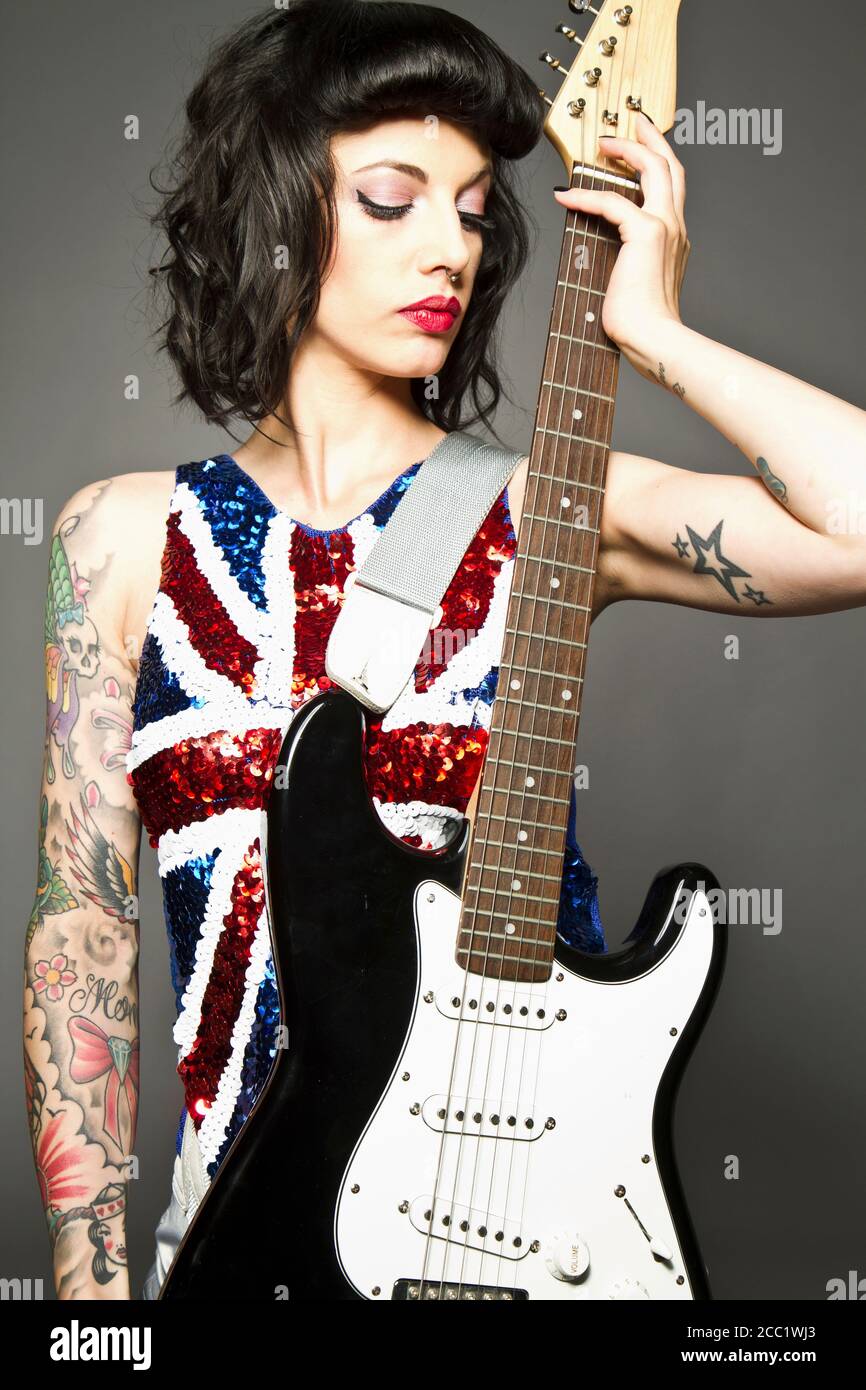 Junge Frau mit Gitarre und Tattoo auf der Hand gegen Grauer Hintergrund Stockfoto