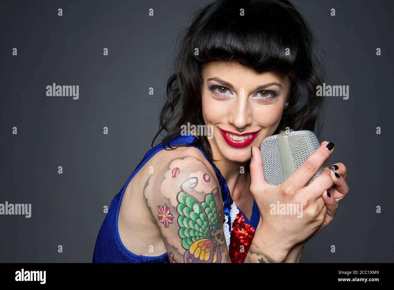 Nahaufnahme einer jungen Frau mit Tattoo auf der Hand vor grauem Hintergrund, Gesang, Porträt Stockfoto