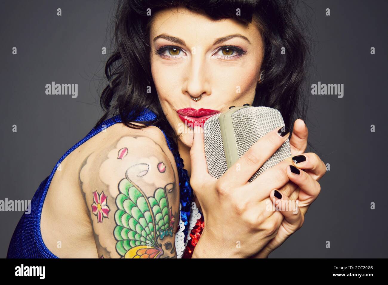 Nahaufnahme einer jungen Frau mit Tattoo auf der Hand vor grauem Hintergrund, Gesang, Porträt Stockfoto