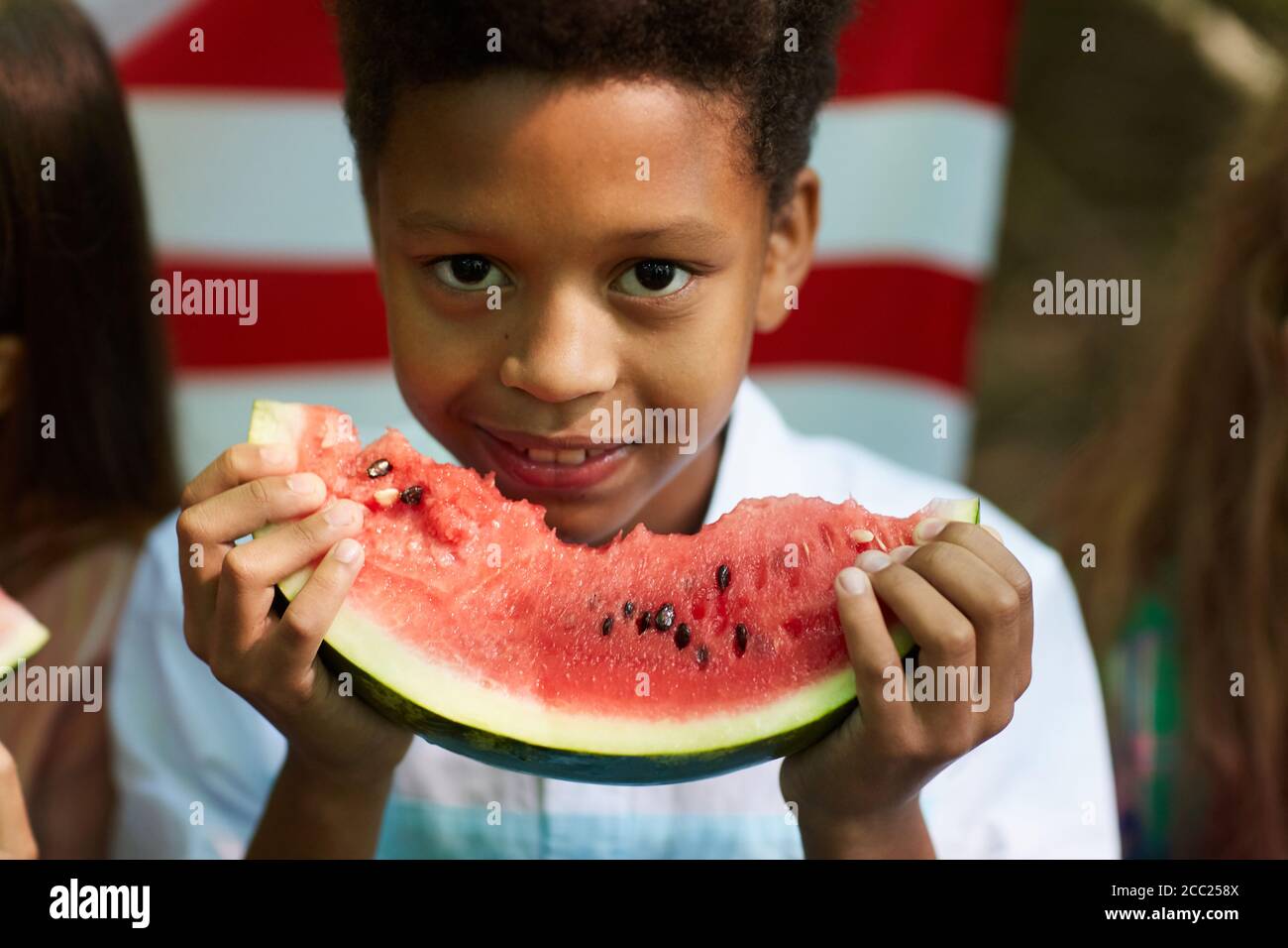 Nahaufnahme Porträt eines lächelnden afrikanischen Jungen hält Wassermelone und Blick auf die Kamera mit amerikanischer Flagge im Hintergrund, kopieren Raum Stockfoto