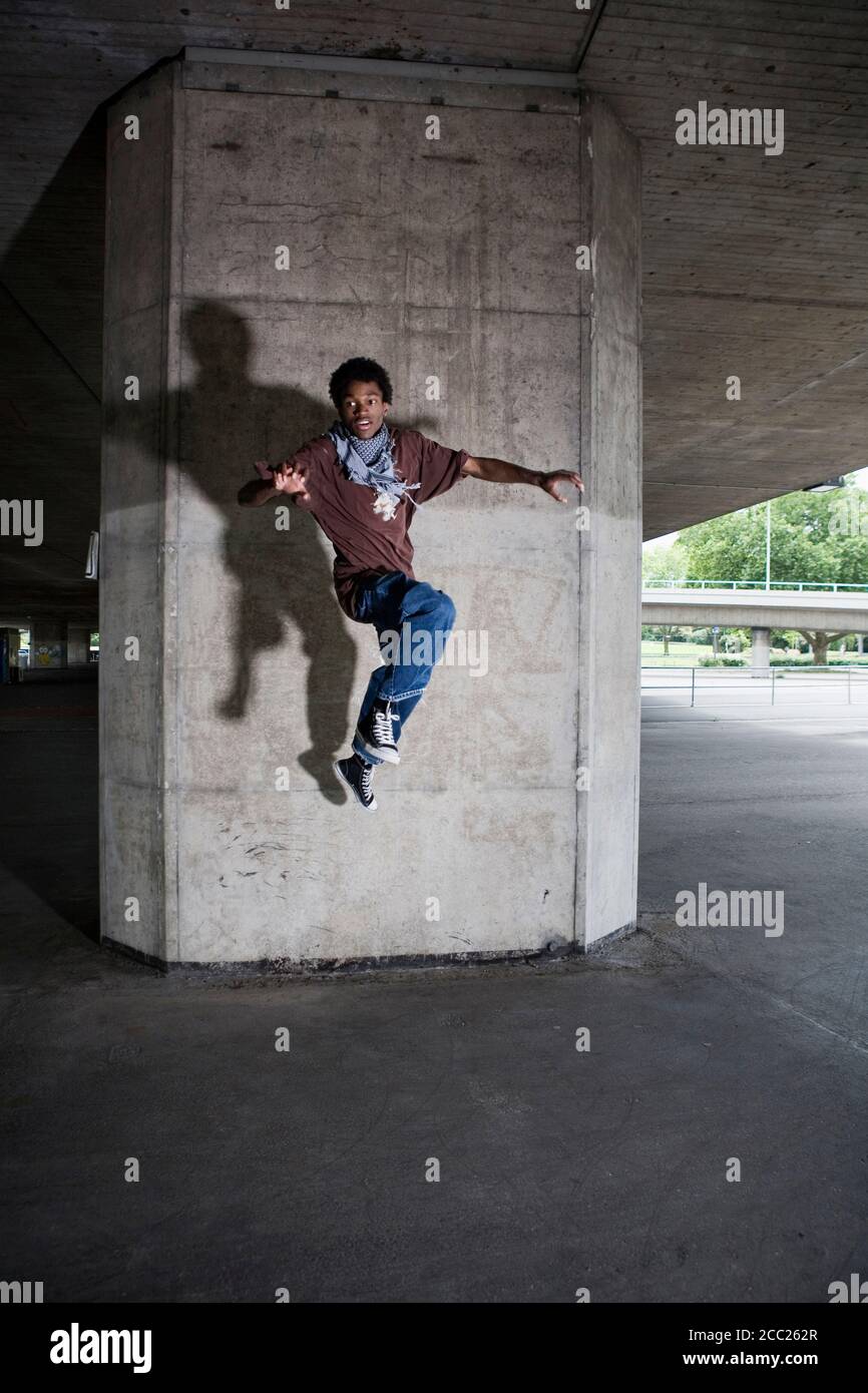Deutschland, Köln, junger Mann springt in die Luft vor Betonwand, Porträt Stockfoto