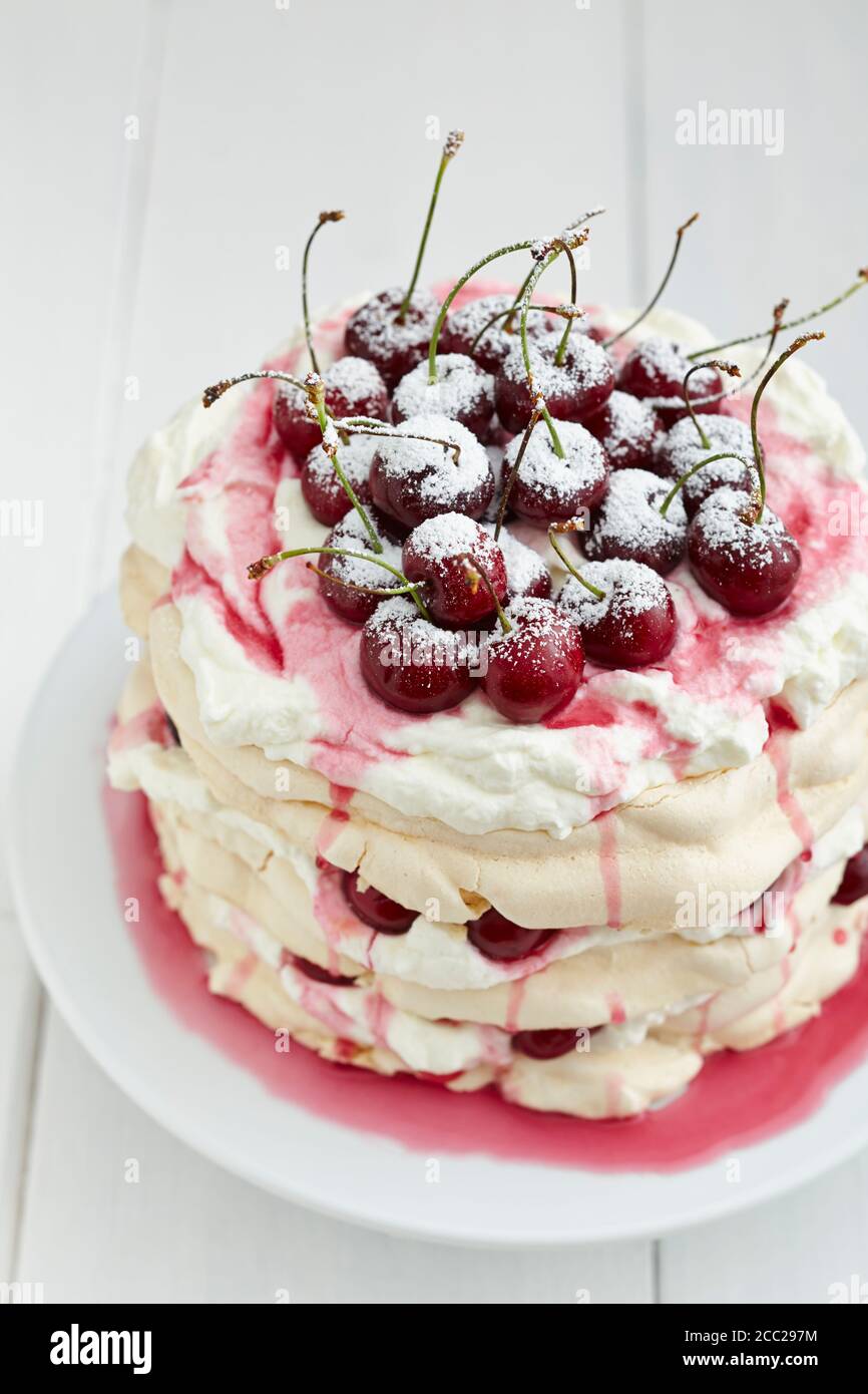 Pavlova mit Schlagsahne, Kirschen, Kirschsauce und Puderzucker auf Kuchenplatte, Nahaufnahme Stockfoto