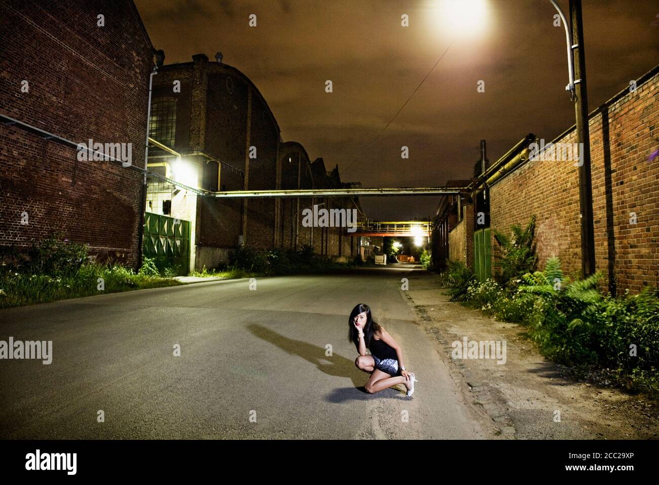 Deutschland, Köln, junge Frau kauert auf leere Straße, Porträt Stockfoto