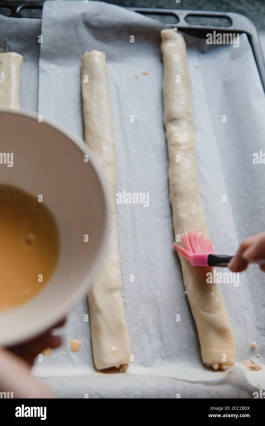 Draufsicht der Person, die rohes Ei auf Brötchen schmiert, während Gebäck wird vorbereitet Stockfoto