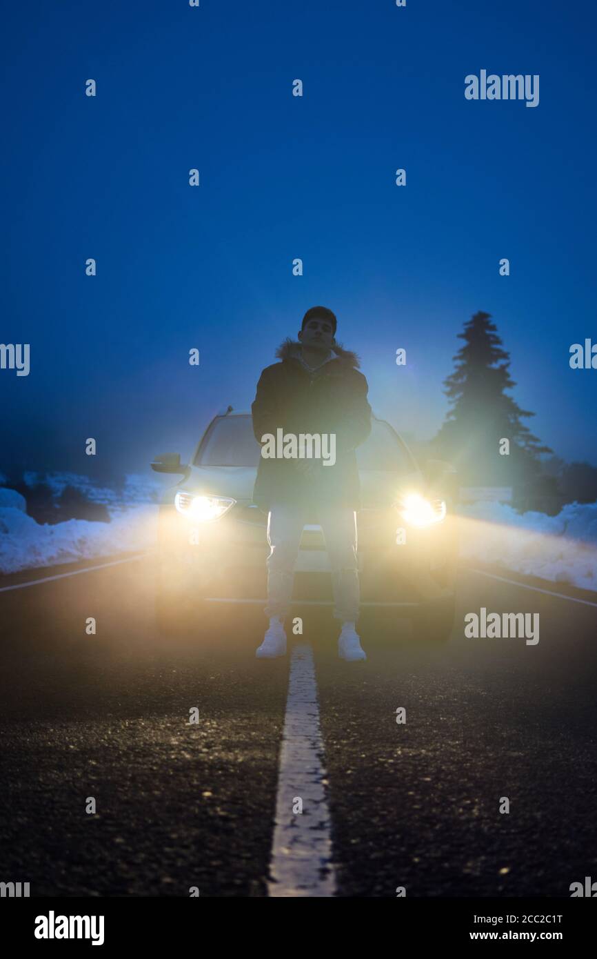 Der junge Mann posiert mit seinem Auto im Hintergrund In einer verschneiten Nacht Stockfoto