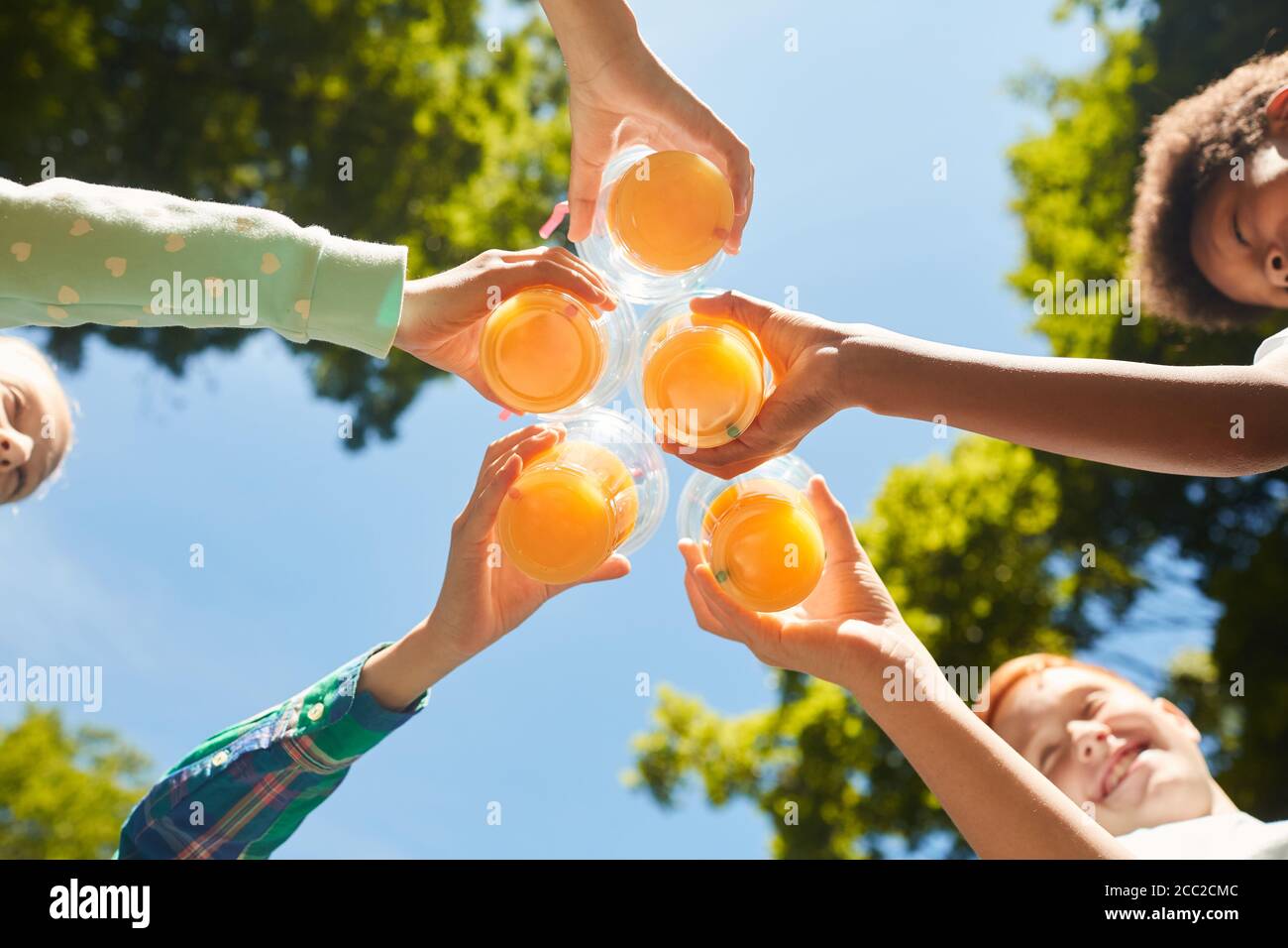 Nahaufnahme von Kindern mit Gläsern mit Orangensaft am blauen Himmel im Freien, Kopierbereich Stockfoto