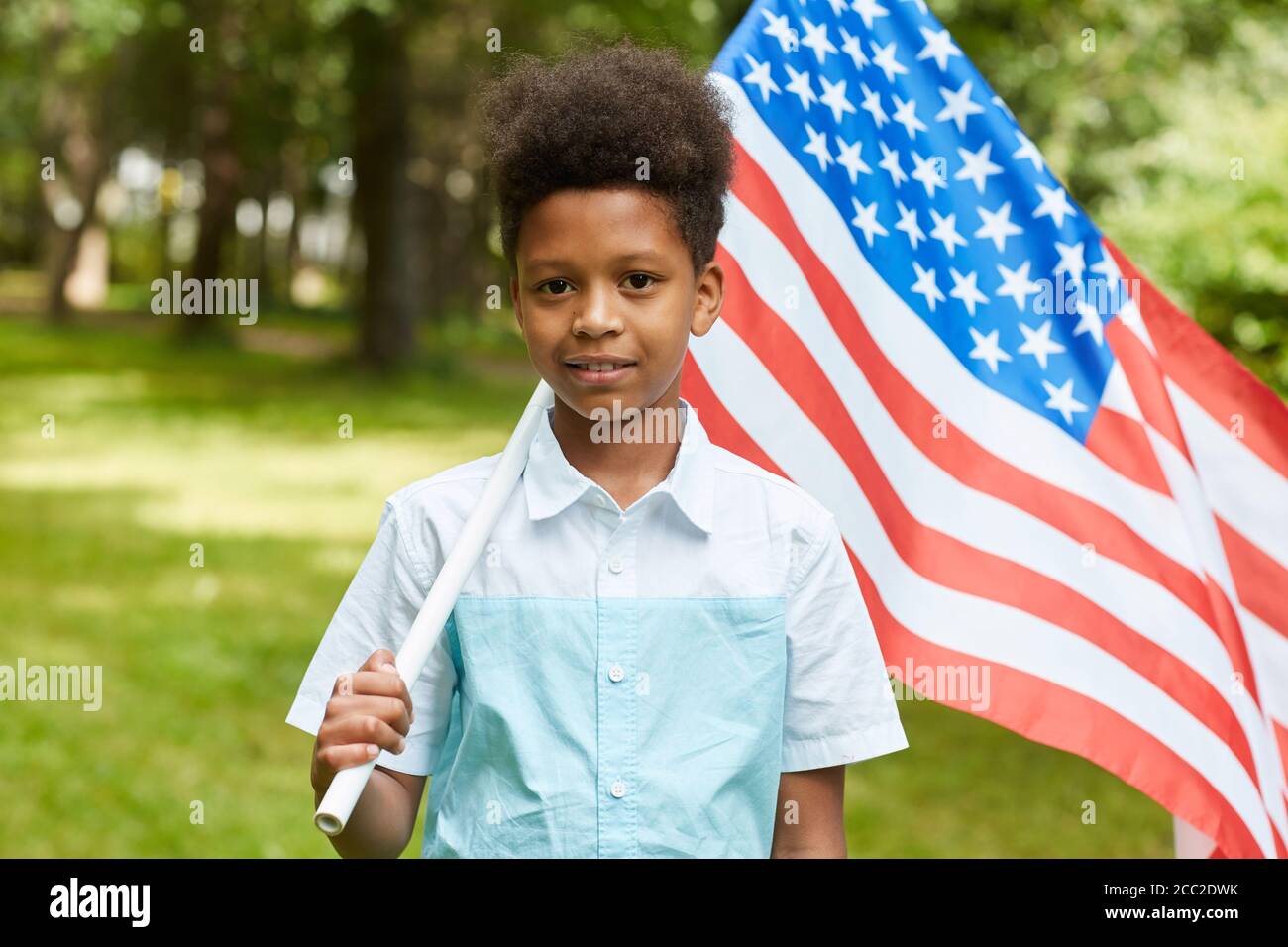 Waist up Porträt von lächelnden afrikanischen Jungen mit amerikanischer Flagge, während im Freien im Park stehen, kopieren Raum Stockfoto