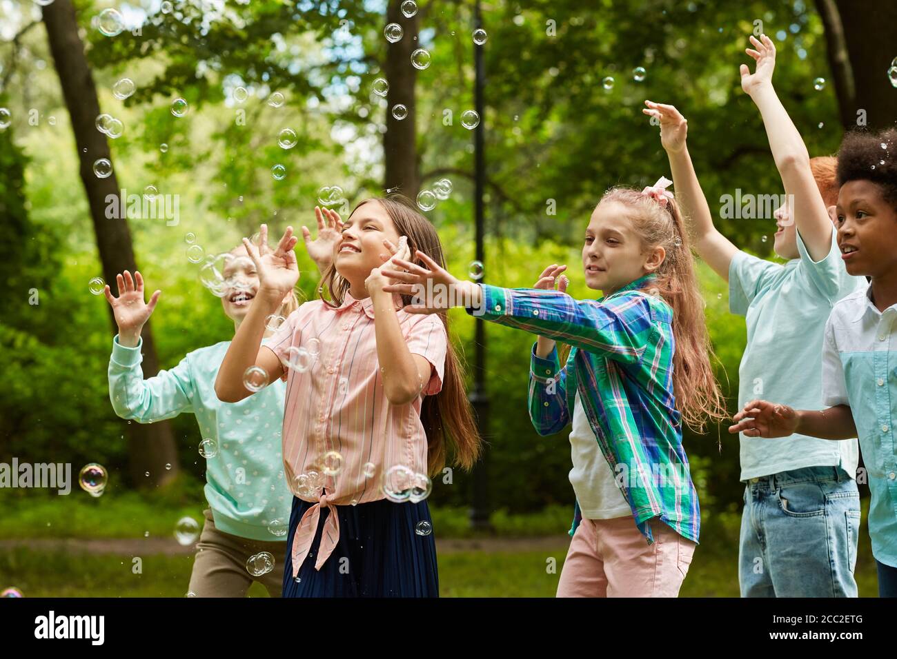 Waist up Porträt der multi-ethnischen Gruppe von sorglosen Kindern laufen Im Park beim Spielen mit Blasen im Freien Stockfoto