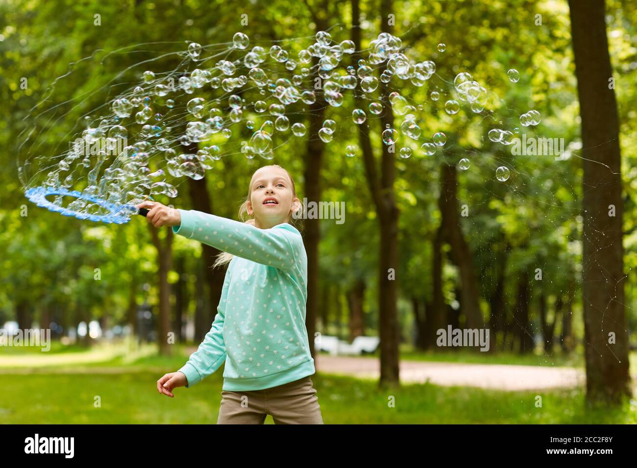 Waist up Porträt von niedlichen Mädchen spielen mit Blasen im Freien im grünen Park hält große Blase Zauberstab, kopieren Raum Stockfoto