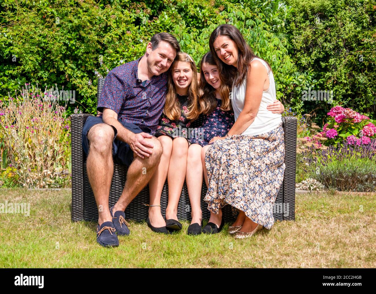 Horizontales Porträt einer jungen Familie, die in ihrem Garten eng beisammen sitzt. Stockfoto