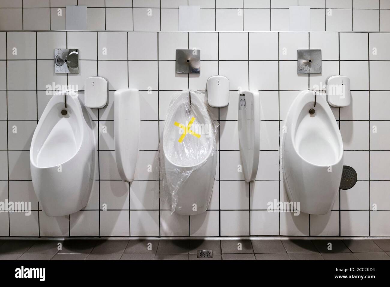Verbotsband und Distanzaufkleber Schild mit Plastikfolie über Das Urinal in einer öffentlichen Toilette für die Menschen zu Folgen Sie der sozialen Distanzierung, um in zu vermeiden Stockfoto