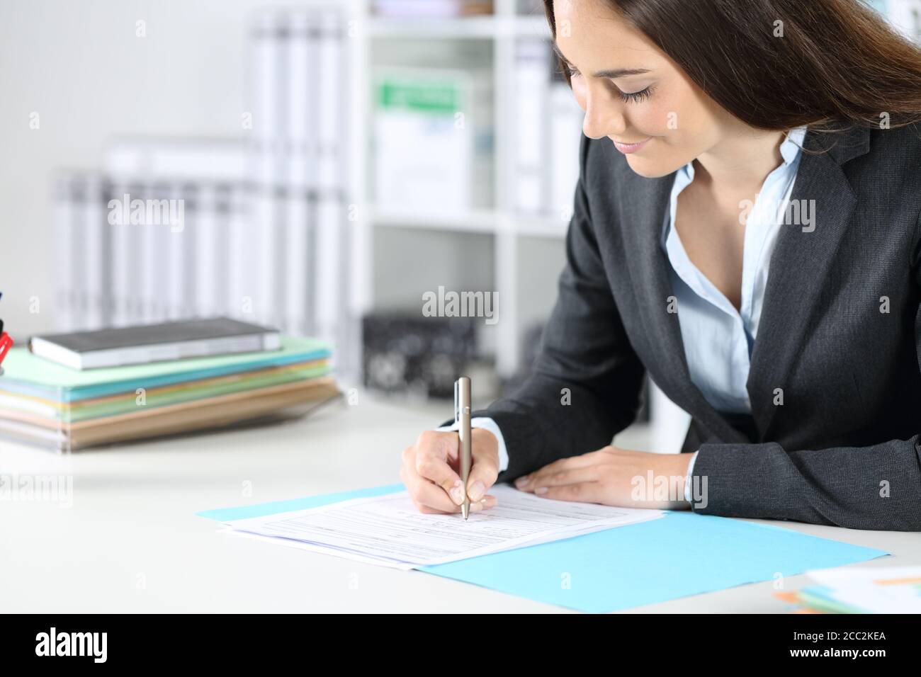 Die Geschäftsführerin, die das Formular ausfüllt, sitzt auf einem Schreibtisch bei Das Büro Stockfoto