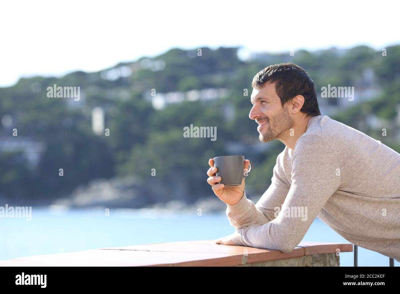 Seitenansicht eines glücklichen Mannes mit Blick auf Kaffee tasse auf einem Balkon am Strand Stockfoto