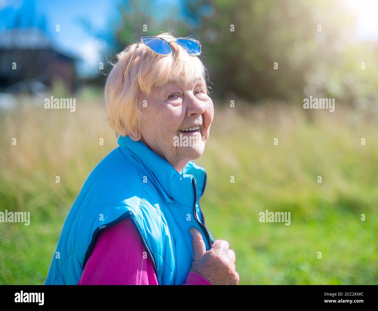 Fröhliche, modische 90-jährige Großmutter mit grauen Haaren und einem Lächeln in der Natur an einem sonnigen Sommertag. Stockfoto