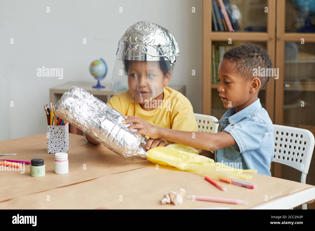 Portrait von zwei afroamerikanischen Jungen, die aus Folie Raum Anzüge machen, während sie Kunst- und Bastelunterricht im Kindergarten oder Entwicklungszentrum genießen, Raum kopieren Stockfoto