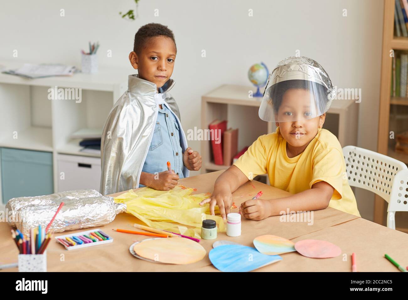 Portrait von zwei afroamerikanischen Jungen, die Astronauten spielen und die Kamera betrachten, während sie Kunst- und Bastelunterricht in der Vorschule oder im Entwicklungszentrum genießen, Stockfoto