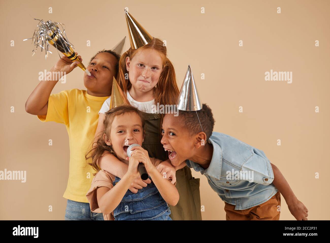 Waist up Porträt von verschiedenen Gruppe von Kindern tragen Partei Hüte schreien zum Mikrofon, während sie vor schlichtem Hintergrund stehen studio Stockfoto