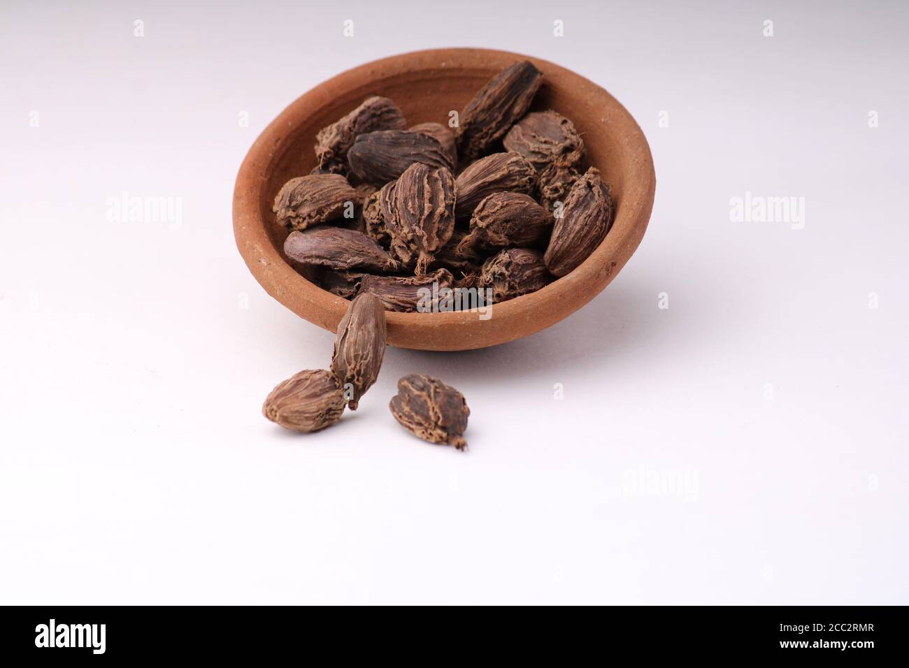 Schwarze Kardamom ganze Samen in einer Schüssel auf weißem Hintergrund indische Gewürz mit Copyspace Stockfoto