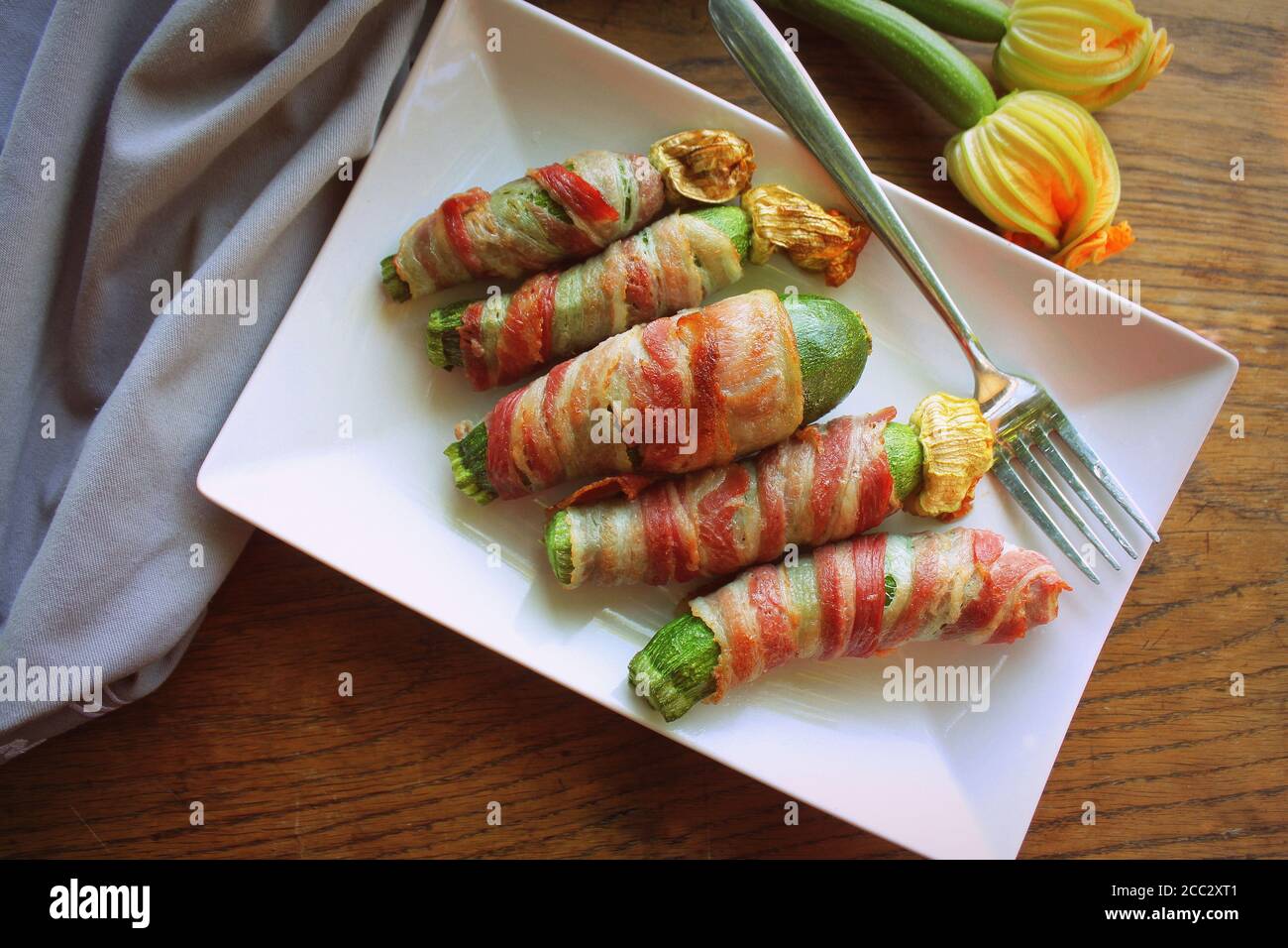 Gegrillte Zucchini-Pommes in einem Speck auf weißem Teller gewickelt Stockfoto
