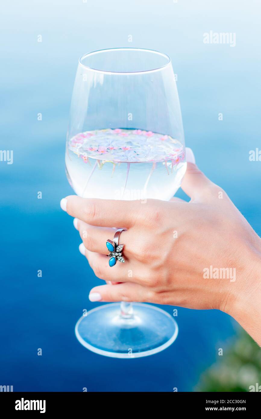 Eine schöne Hand mit einem Ring hält ein Glas vor dem Hintergrund des Meeres. Stockfoto