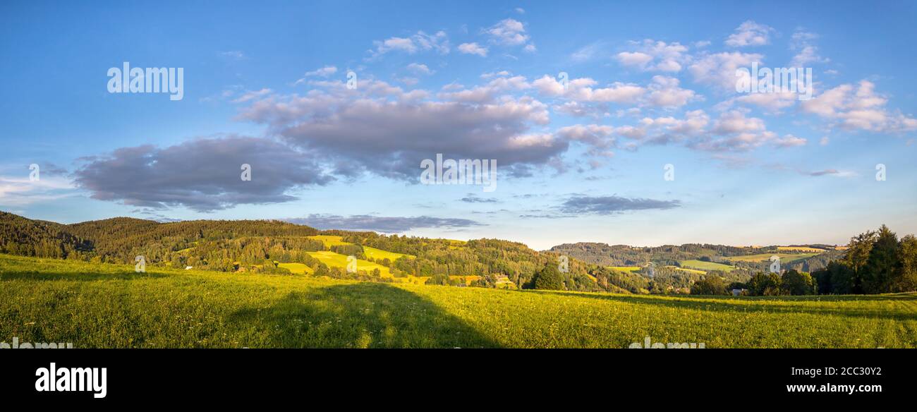 Schöne Landschaft mit Wiesen, Bäumen, Wäldern, im Hintergrund bewaldeten Hügeln und blauen Himmel mit Wolken Stockfoto