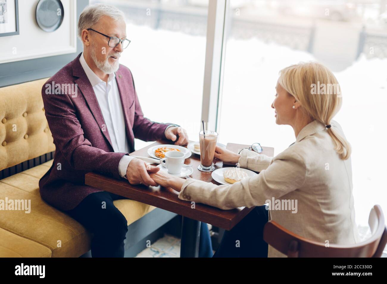 Wunderschöne reife stilvolle Mann zeigt seine Zuneigung, Gefühl, eine schöne blonde Frau beim Tee trinken im Café. Close up Seitenansicht Foto Stockfoto