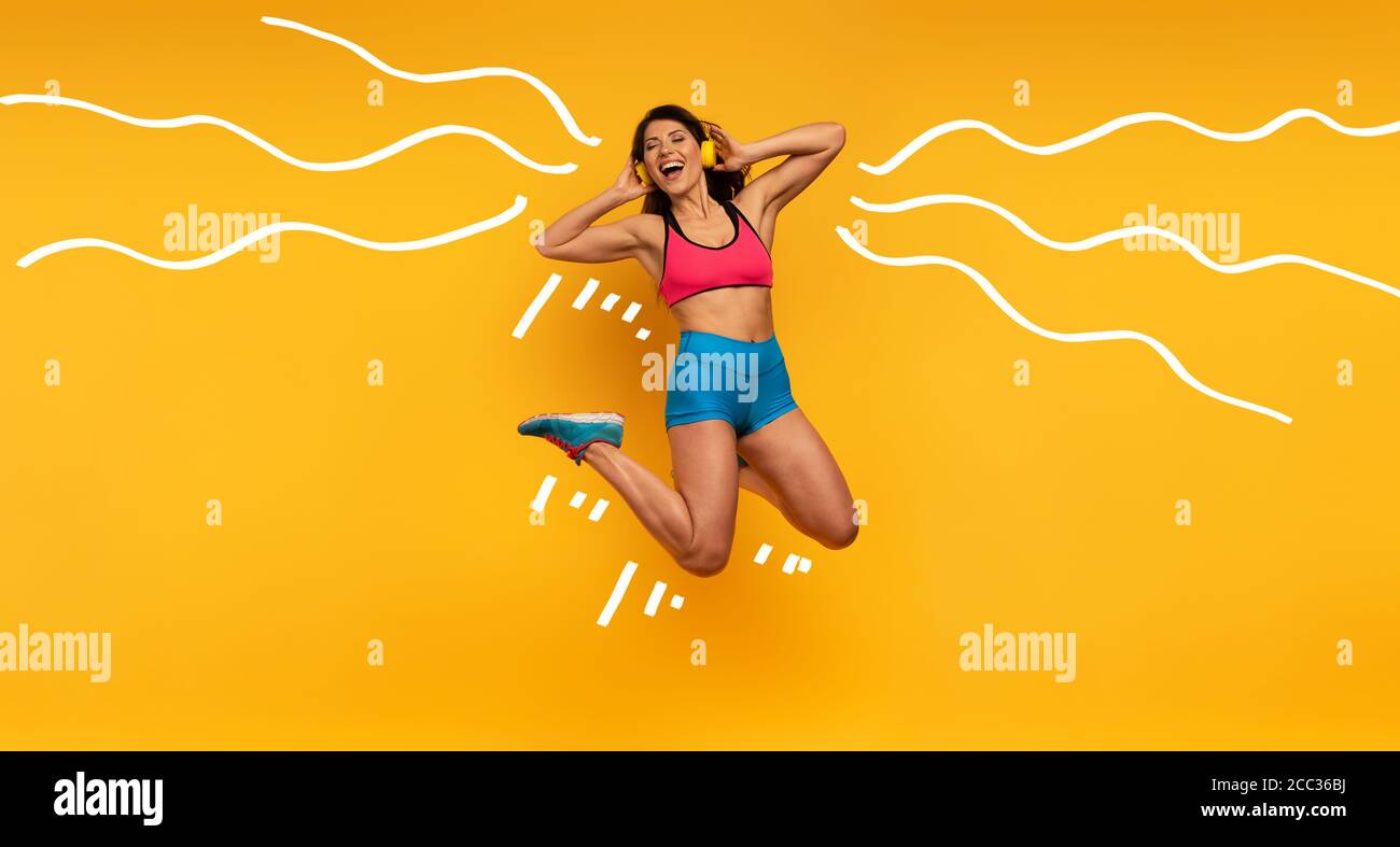 Sport Frau springt auf einem gelben Hintergrund und hören Sie Musik. Fröhlicher und freudiger Ausdruck. Stockfoto