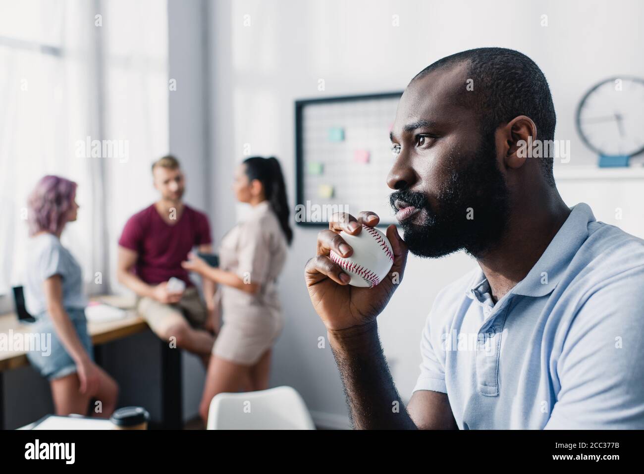Selektiver Fokus des nachdenklichen afroamerikanischen Geschäftsmannes, der Baseballball hält Im Büro Stockfoto