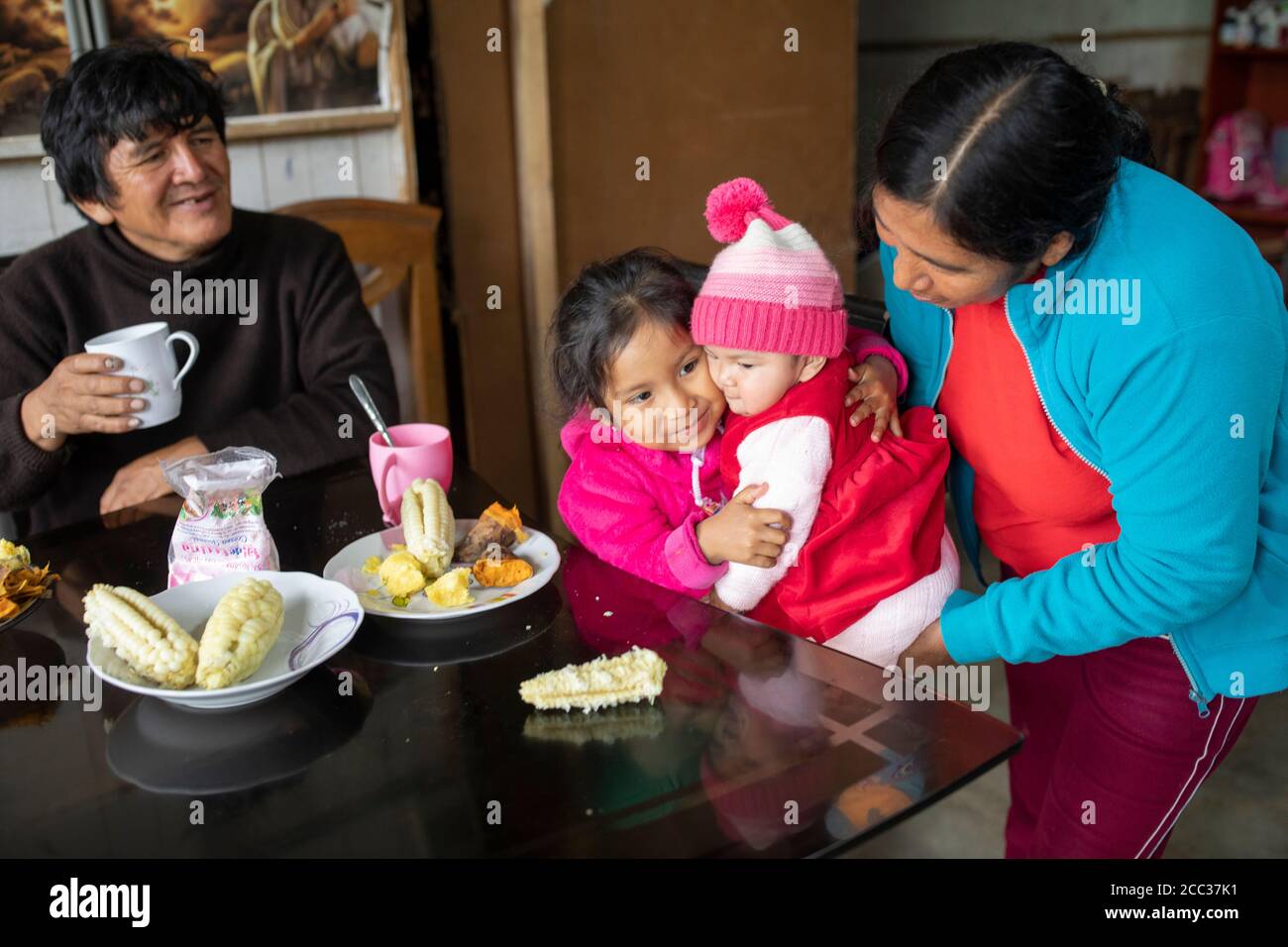 Ein Mädchen umarmt ihre kleine Schwester am Frühstückstisch mit Mais und Süßkartoffeln in Manchay Alto, Bezirk Pachamac, Peru. Stockfoto