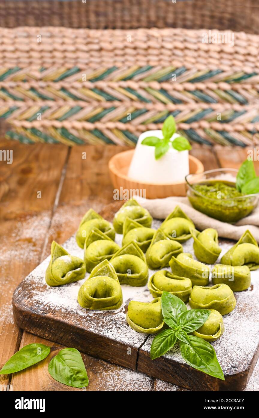 Tortellini e Tortelloni typische Gerichte emilia italien. Food Hintergrund mit hausgemachten rohen italienischen Tortelloni und Zutaten für grünes Pesto auf Holzhintergrund . Weitwinkelansicht. Speicherplatz kopieren. Stockfoto