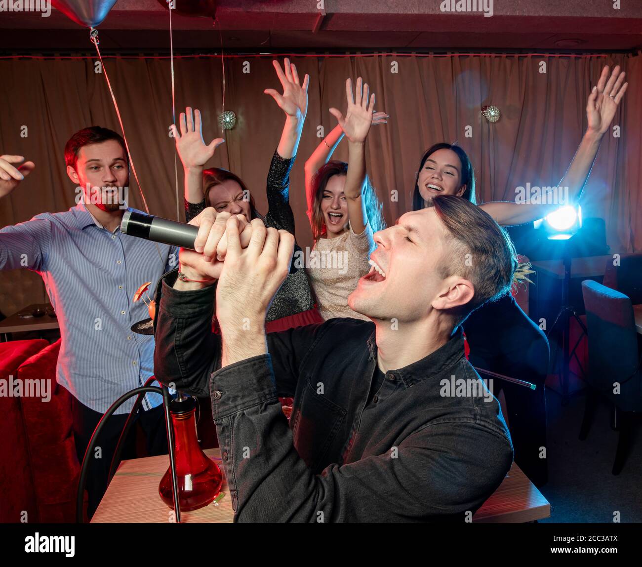 Der junge Kaukasier feiert Geburtstag in der Karaoke-Bar, singt im Mikrofon, schaukelt und chillt im Sängerclub. Stockfoto