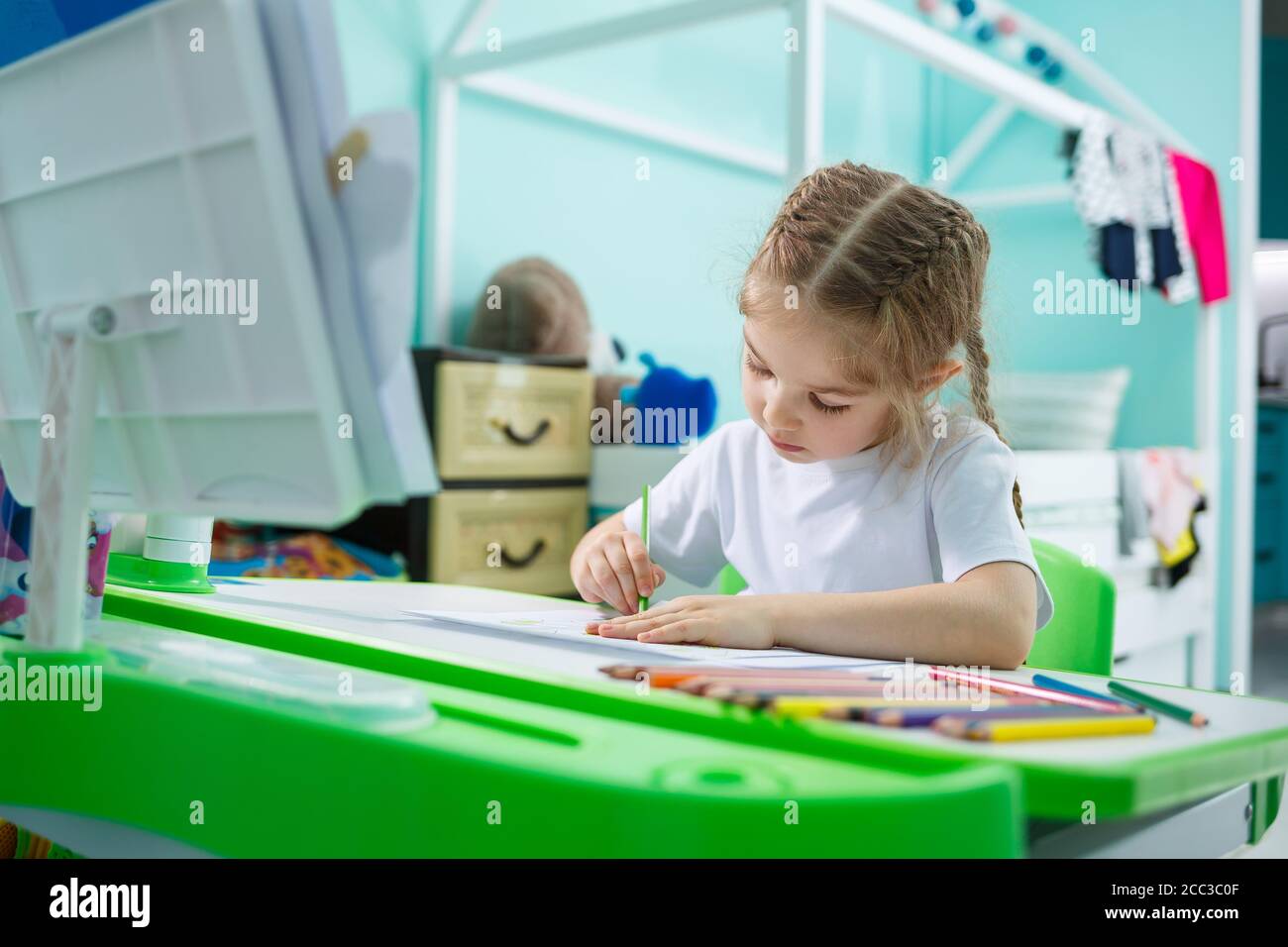 Portrait eines niedlichen kleinen Mädchen, das auf die Kamera und lächelt beim Zeichnen von Bildern oder Hausaufgaben, sitzen an einem Tisch im Inneren des Hauses Stockfoto