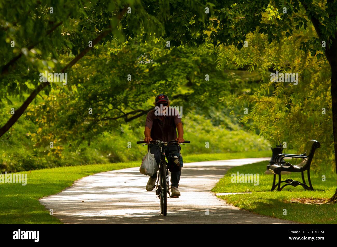 Frederick, MD, USA 08/14/2020: Ein älterer Kaukasier mit Baseballmütze fährt an einem sonnigen Tag mit dem Fahrrad durch den Baker Park. Er trägt Taschen Stockfoto