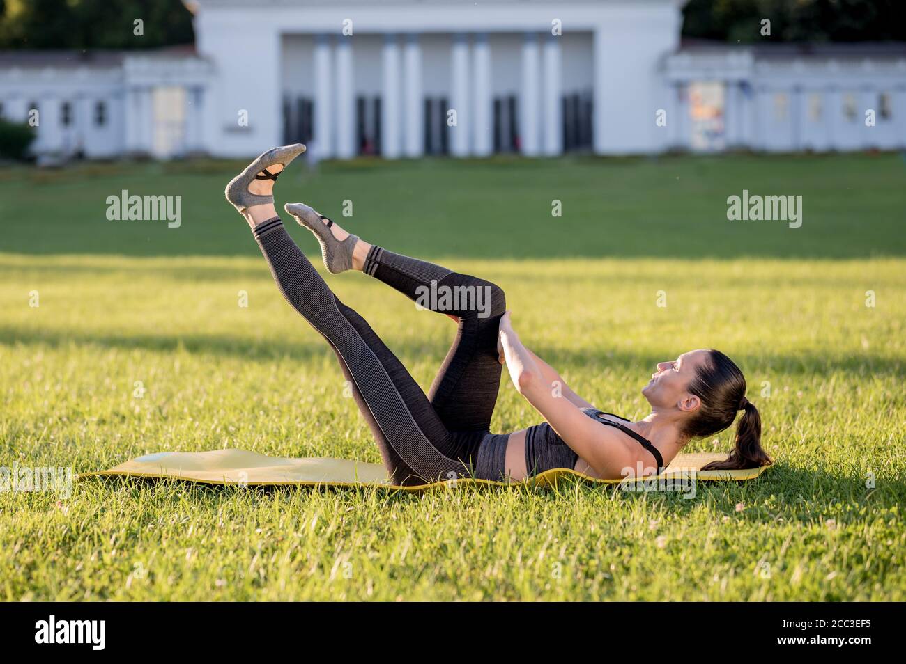 Schöne junge Frau liegt auf einer gelben Matratze, Pose, während das Tragen eines engen Sport-Outfit im Park tun Pilates oder Yoga, Single Bein Stretch inter Stockfoto