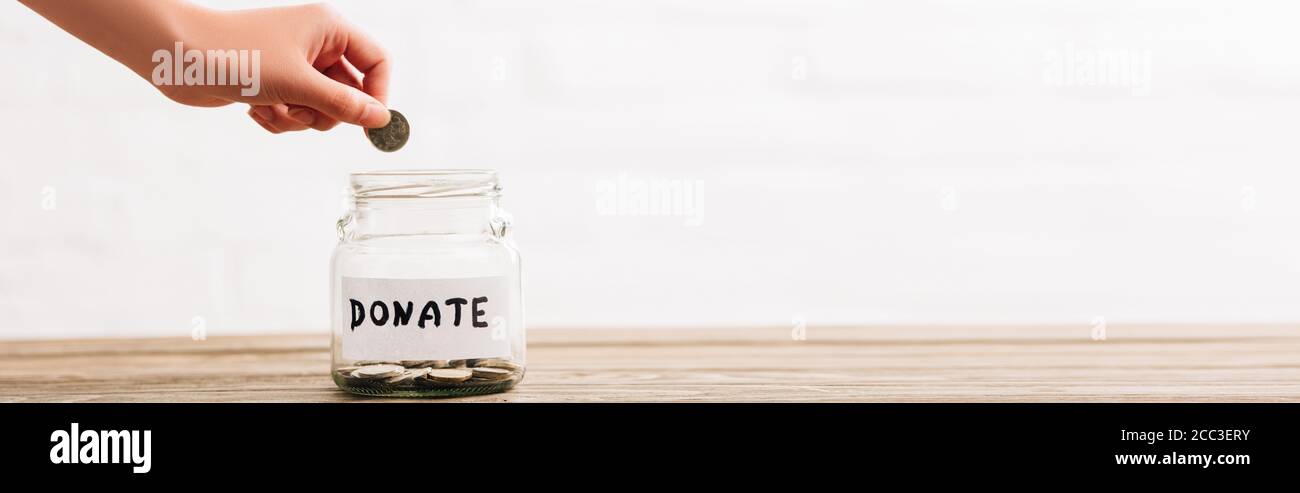 Beschnittene Ansicht der Frau Putting Münze in Penny jar mit spenden Schriftzug auf Holzfläche auf weißem Hintergrund, Panorama-Aufnahme Stockfoto