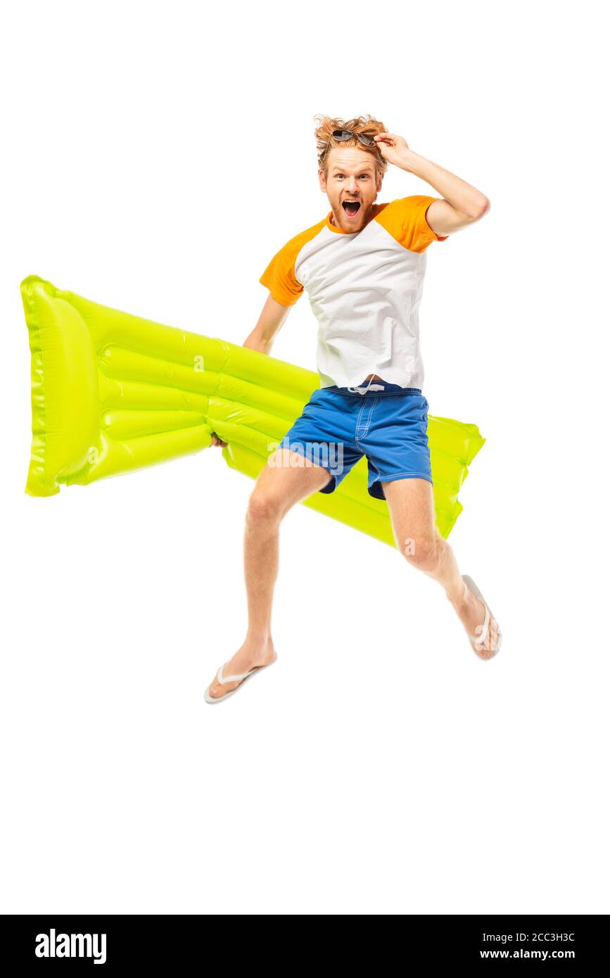 Aufgeregt Mann hält Sonnenbrille und aufblasbare Matratze beim Springen isoliert Auf Weiß Stockfoto