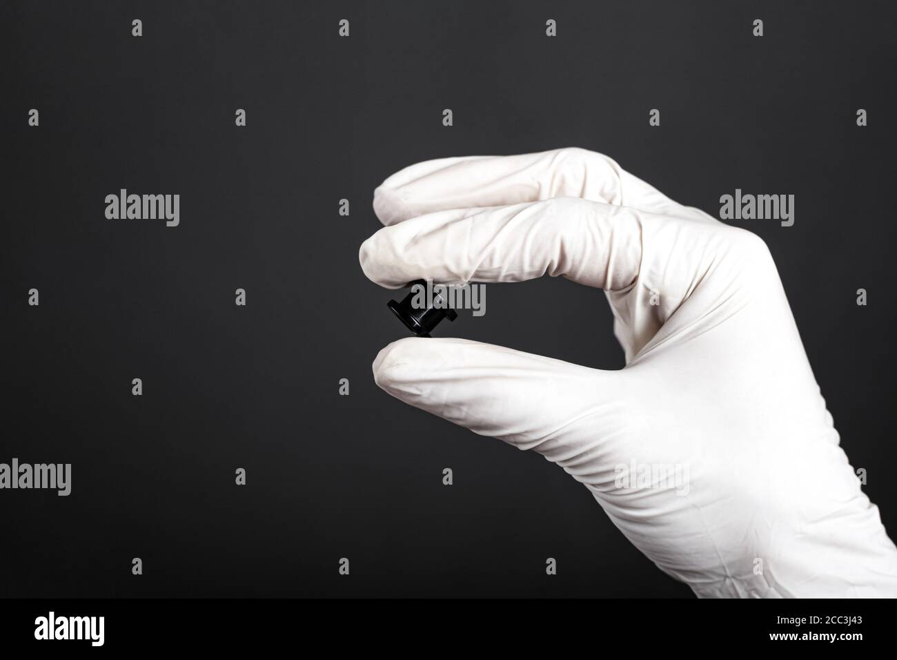 Schwarzer Ohrtunnel in der Hand mit weißem Einweghandschuh auf dunklem Hintergrund Nahaufnahme, Piercing, Ohrschmuck. Stockfoto