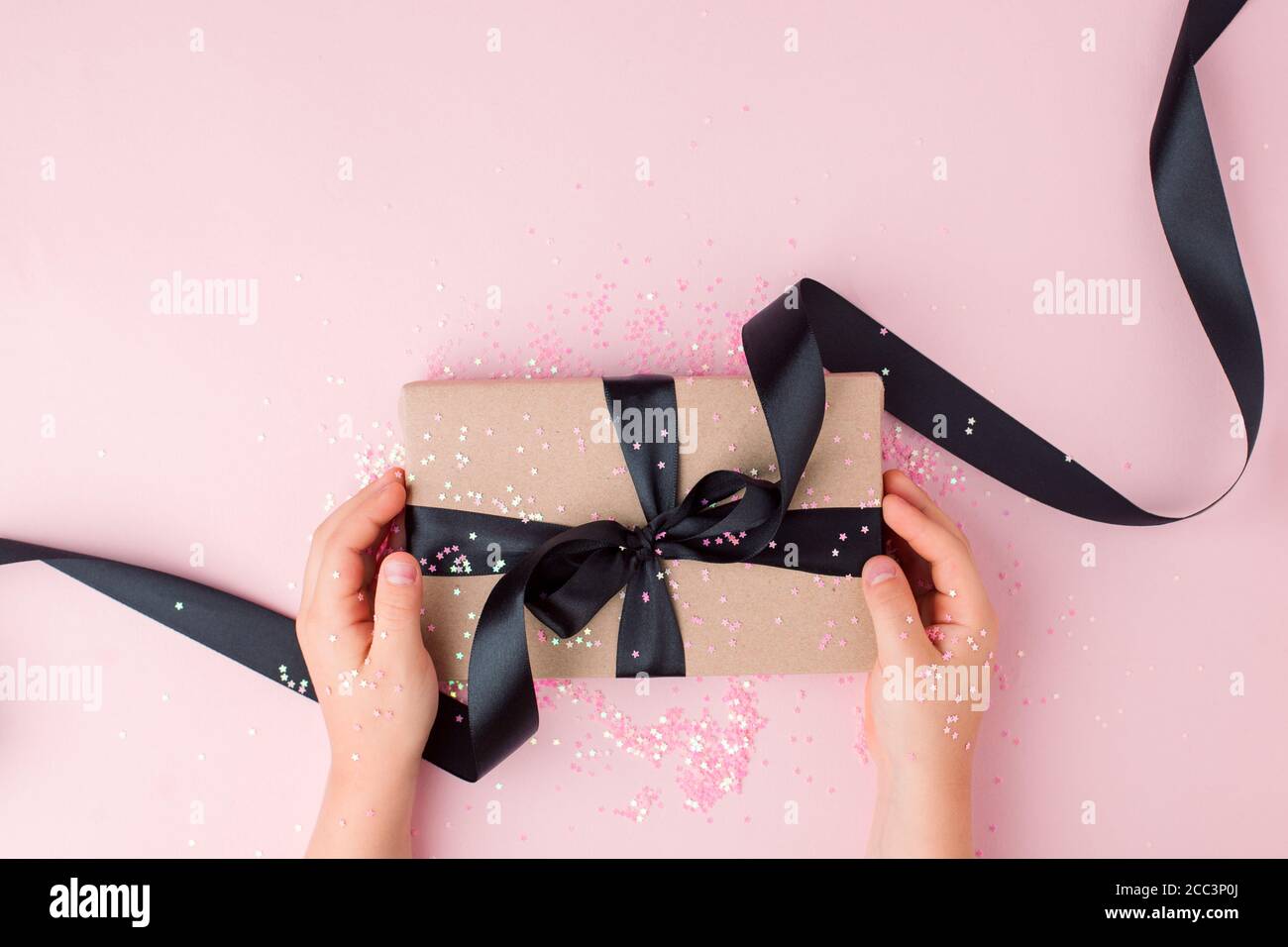 Kinder Hande Halten Geschenk Mit Schwarzer Schleife Auf Pastellrosa Hintergrund Festliche Kulisse Fur Feiertage Geburtstag Valentinstag Muttertag Weihnachten N Stockfotografie Alamy